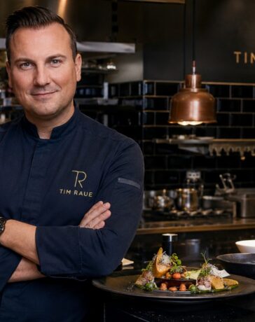 Tim Raue in einer modernen Sterneküche mit einem kunstvoll angerichteten Gourmetgericht.